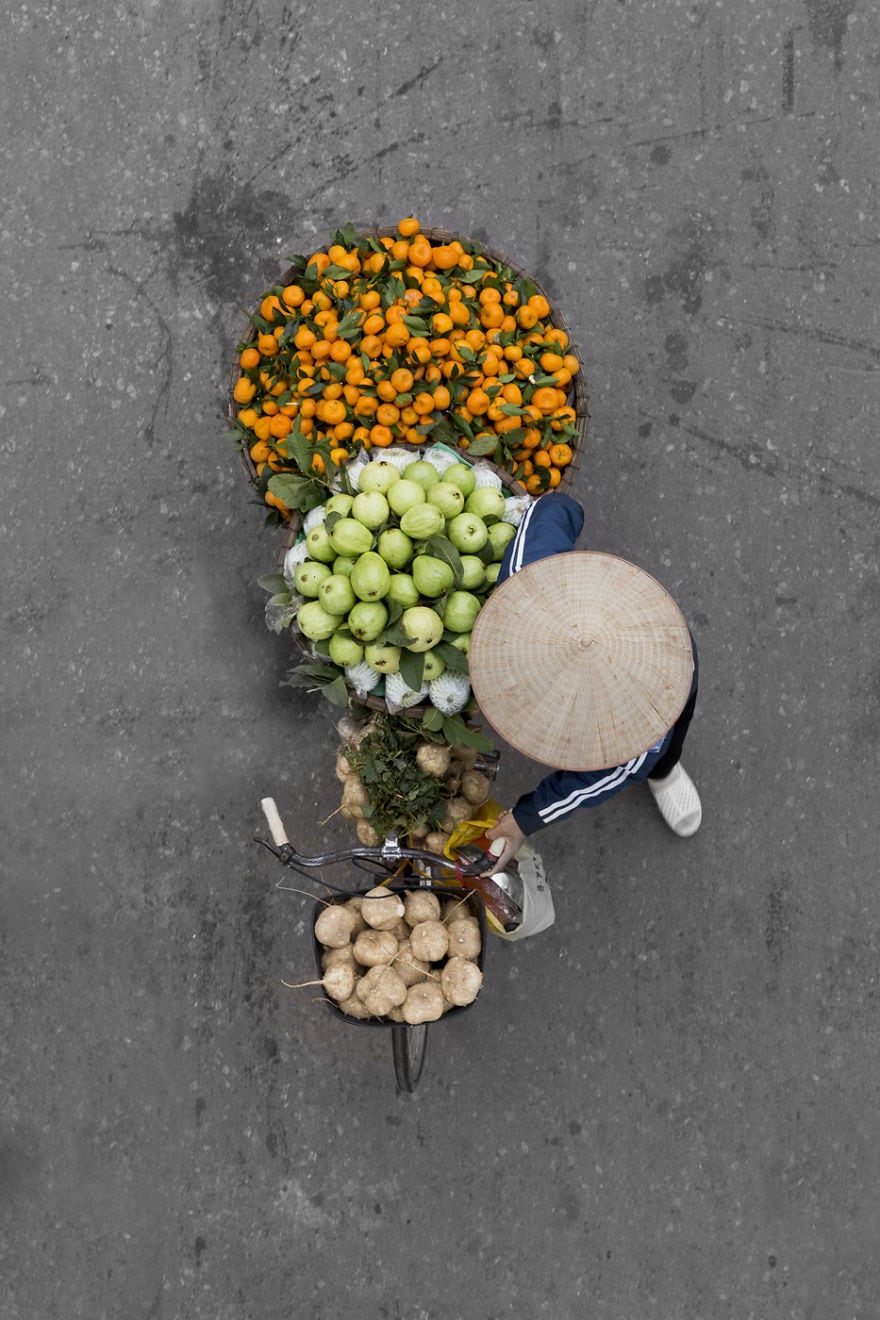 Người gánh hàng rong nhìn từ trên cao, đội nón lá giữa những giỏ cam, táo và rau củ